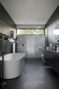 Contemporary bathroom features a minimalist freestanding white tub with sleek, black floor tiles